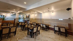 Un restaurant spacieux doté d’un sol en marbre, de nombreuses tables et chaises, de ventilateurs de plafond et d’un éclairage encastré.