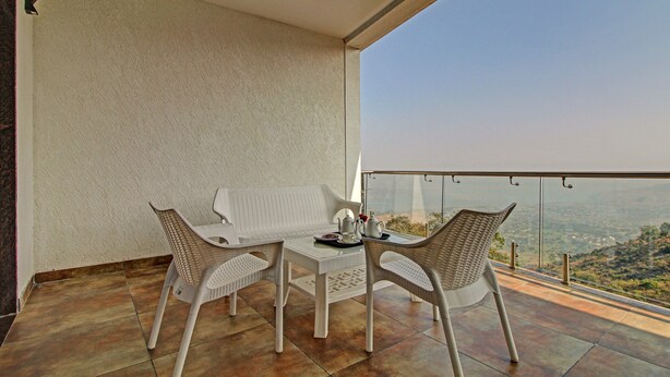 Un balcon avec une table et deux chaises, une vue sur un paysage lointain et un ciel dégagé.