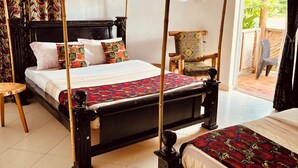 A room with two beds, each with a canopy, a wooden headboard, and a patterned bedspread. There is a chair with a cushion and a small table beside the beds. - Rafiki Safari Lodge Bwindi (Bwindi)