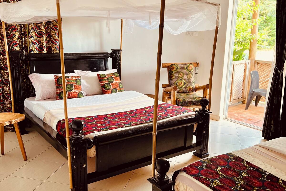 A room with two beds, each with a canopy, a wooden headboard, and a patterned bedspread. There is a chair with a cushion and a small table beside the beds.