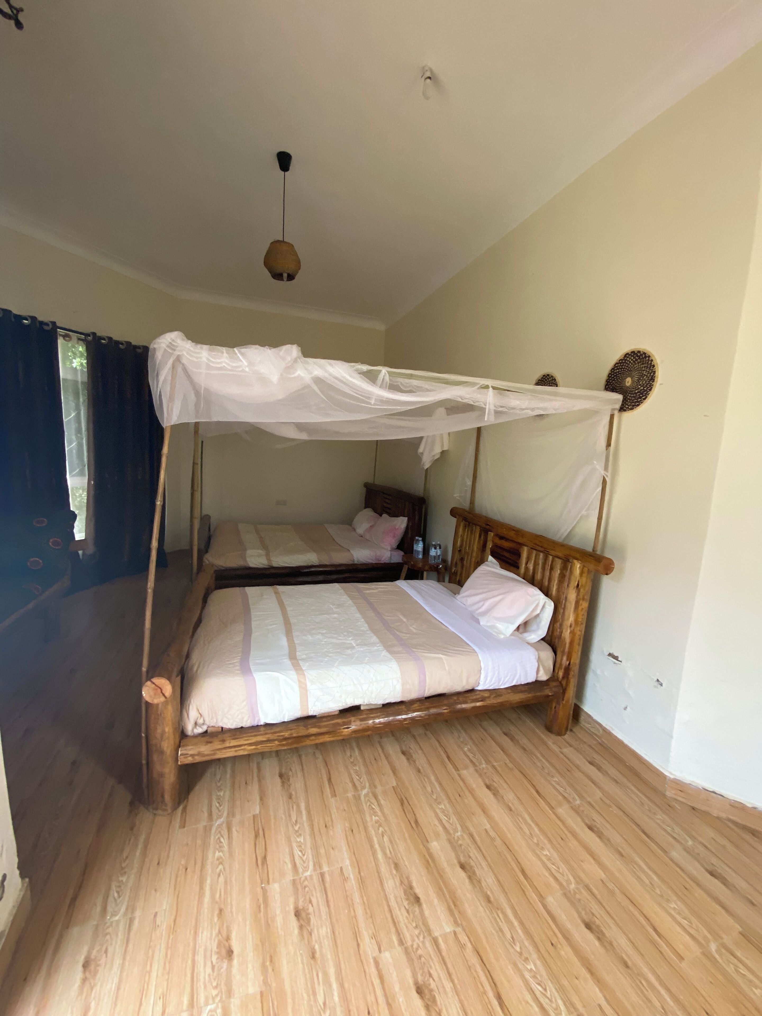 A room with two wooden beds, each with a canopy. The room has a wooden floor and a ceiling fan.