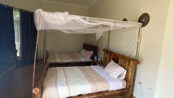 A room with two wooden beds, each with a canopy. The room has a wooden floor and a ceiling fan.