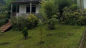 A small house with a sloped roof, surrounded by lush greenery and a mountainous backdrop. - Rafiki Safari Lodge Bwindi (Bwindi)