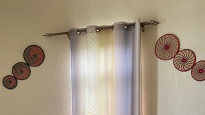 A room with a curtain, a small table with a bottle, and a patterned chair. - Rafiki Safari Lodge Bwindi (Bwindi)