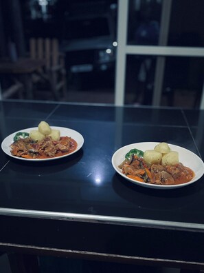 Two plates of stew with potatoes on a reflective black table.