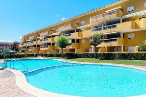 Un immeuble jaune à plusieurs étages, doté de balcons, d’une piscine et surplombant un ciel d’un bleu limpide.