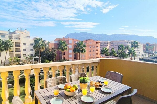 A balcony with a table set for breakfast, overlooking a cityscape with buildings and palm trees.