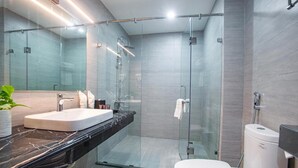 Un baño moderno con ducha de vidrio, inodoro blanco y encimera de mármol con lavamanos.
