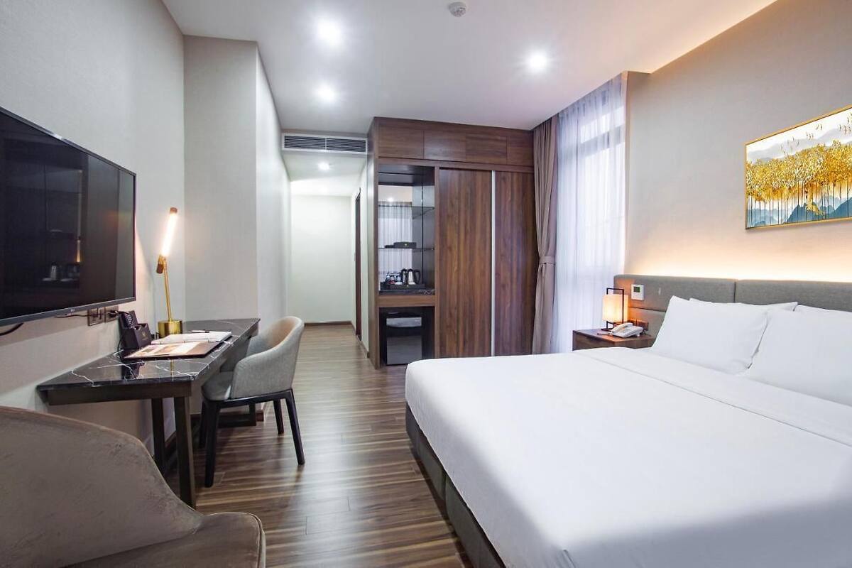 A hotel room with a bed, a desk with a chair, a TV, a wardrobe, and a painting on the wall.