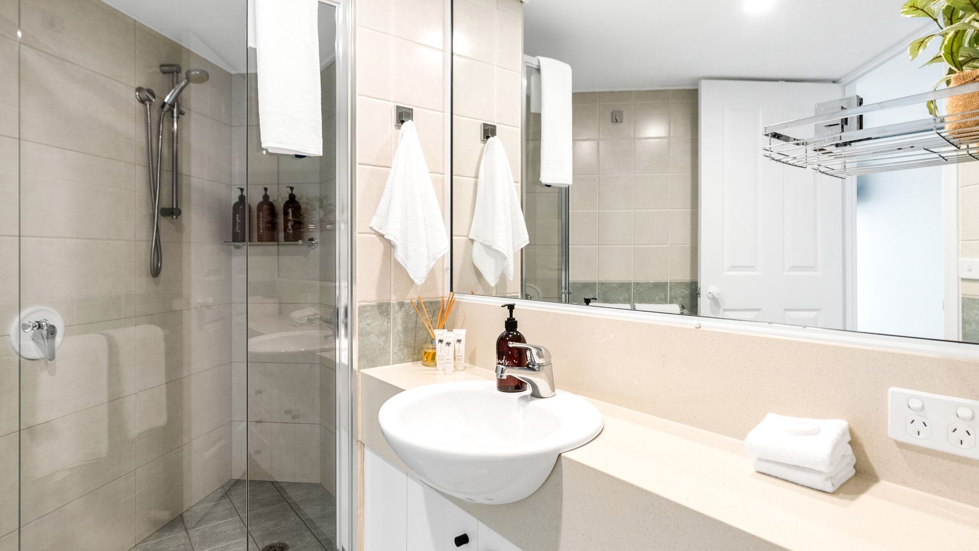 A modern bathroom with a glass shower enclosure, a white sink, and a large mirror.