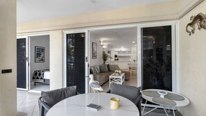 A modern living space with a dining area, a sofa, and a kitchen visible through glass doors.
