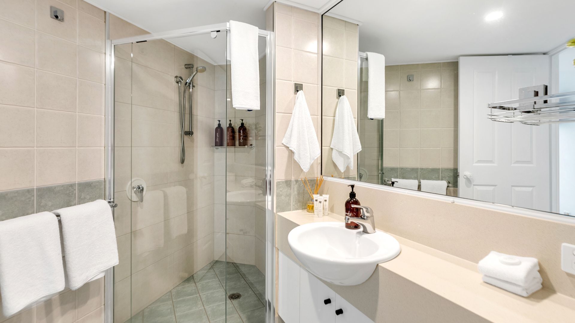 A modern bathroom with a glass-enclosed shower, a white sink, and a large mirror.