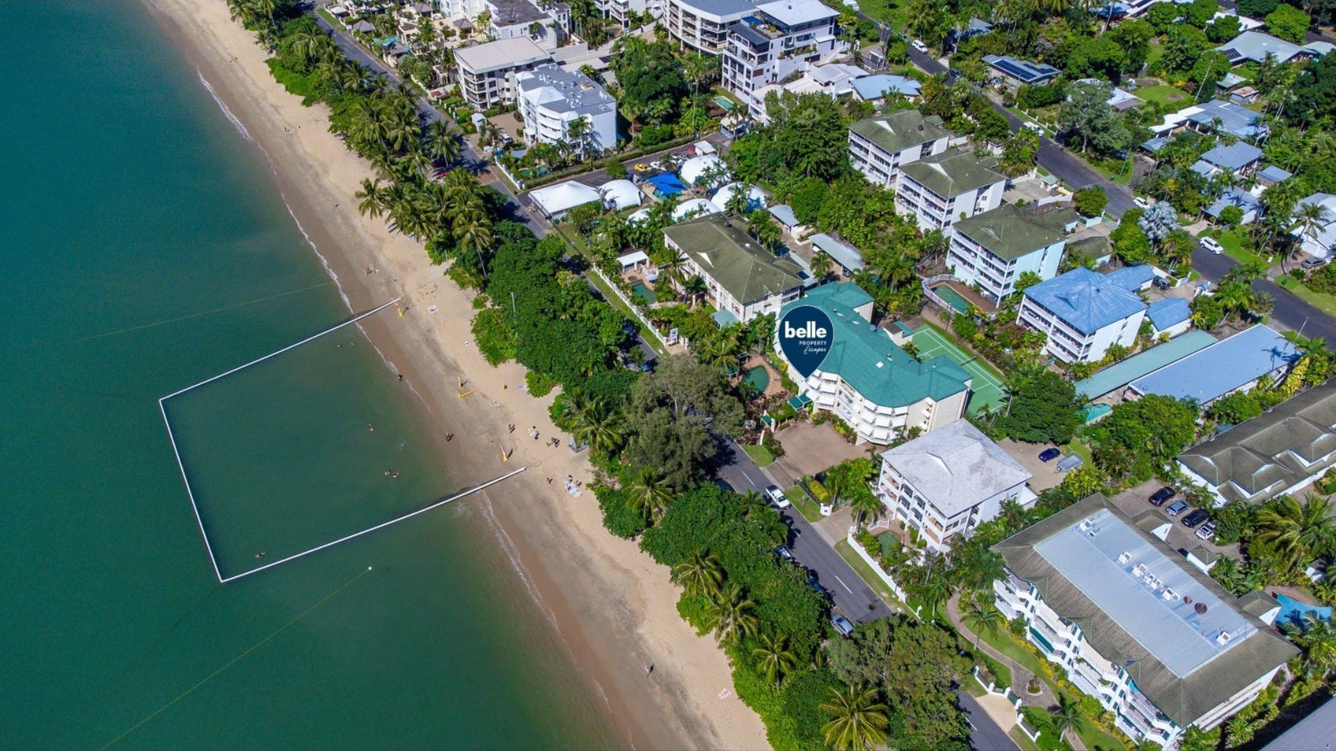 An aerial view of a coastal hotel with a beach, multiple buildings, and a tennis court.