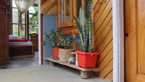 Een houten interieur met een bank waarop potplanten staan, een bed met een rode deken en een raam met een gordijn.