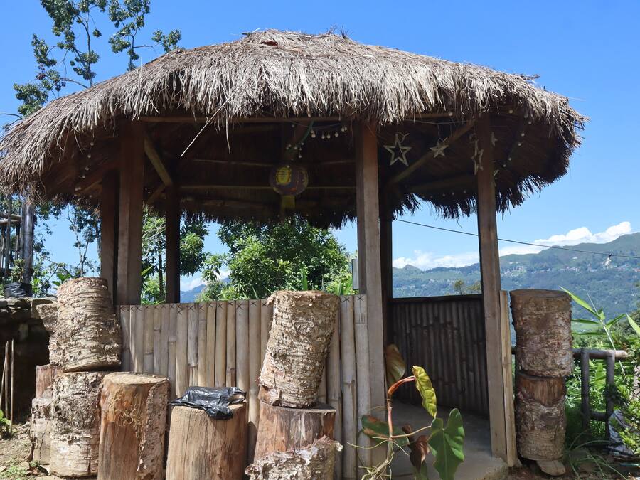 Una estructura de madera rústica con techo de paja, rodeada de paisajes naturales y montañas al fondo.