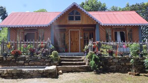 Een houten huis met een rood dak, een stenen muur en een bord met de tekst 'PENUEL HOMESTAY'.