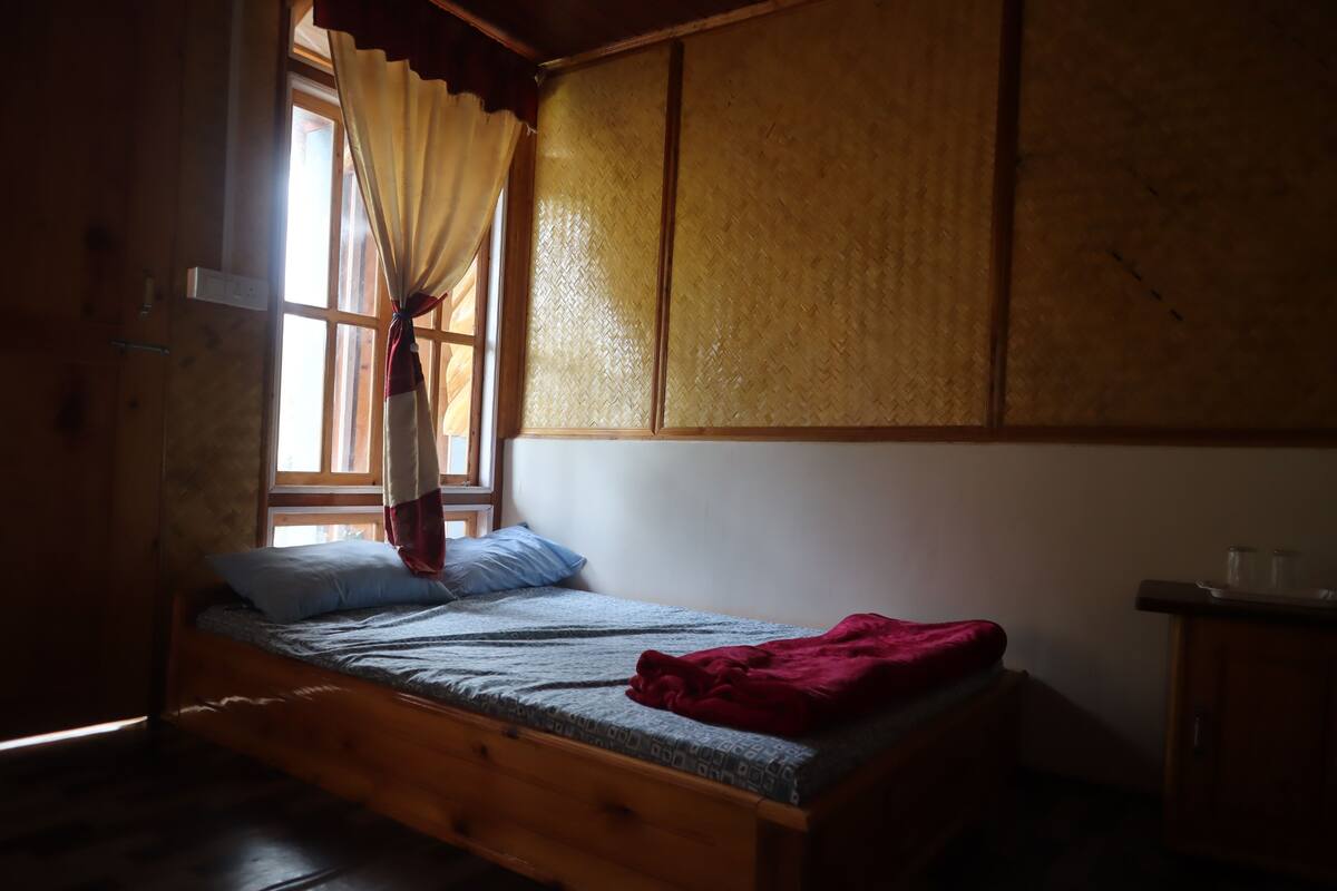 Un lit simple avec un cadre en bois, une fenêtre avec des rideaux et une armoire en bois.