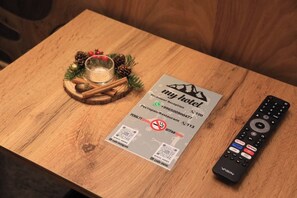 Een houten tafel met een hotel receptiekaart, een afstandsbediening en een glas water met kaneelstokjes en dennenappels.