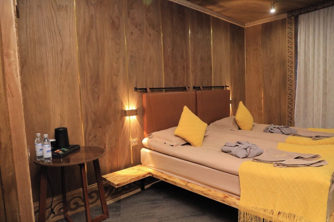 A wooden-paneled room with a bed, a small table with toiletries, and a bench.