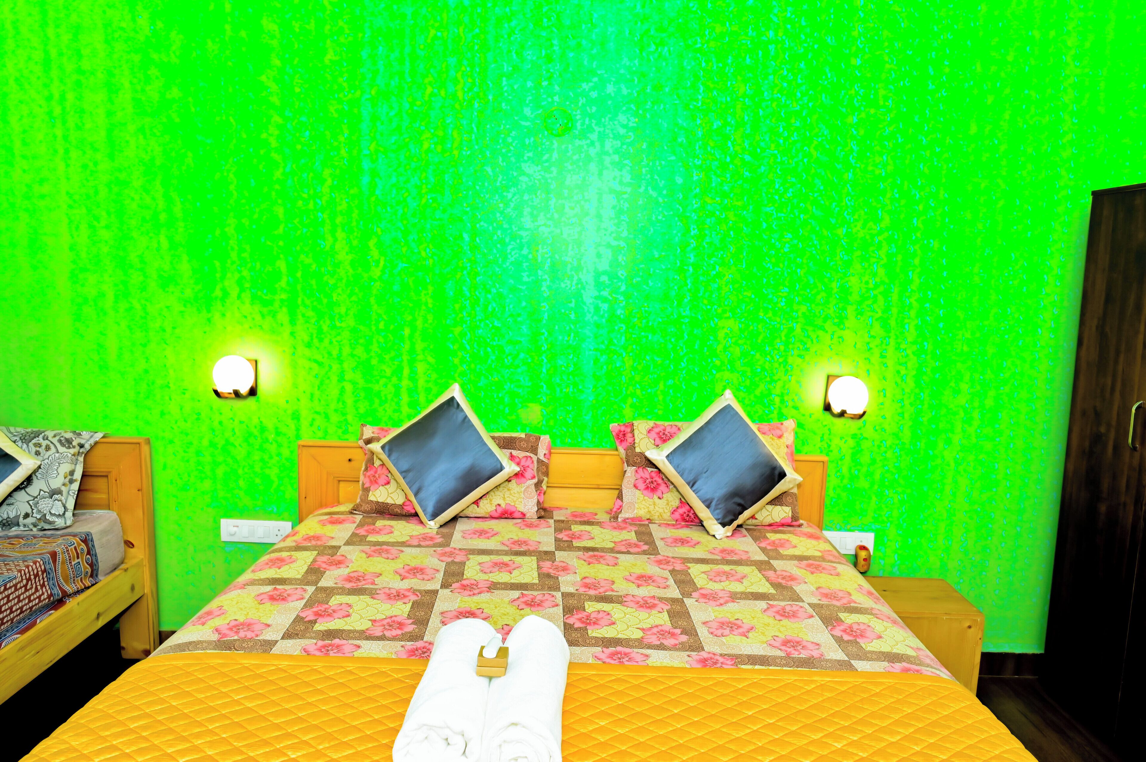 A hotel room with a green textured wall, two beds with floral bedding, and two bedside lamps.