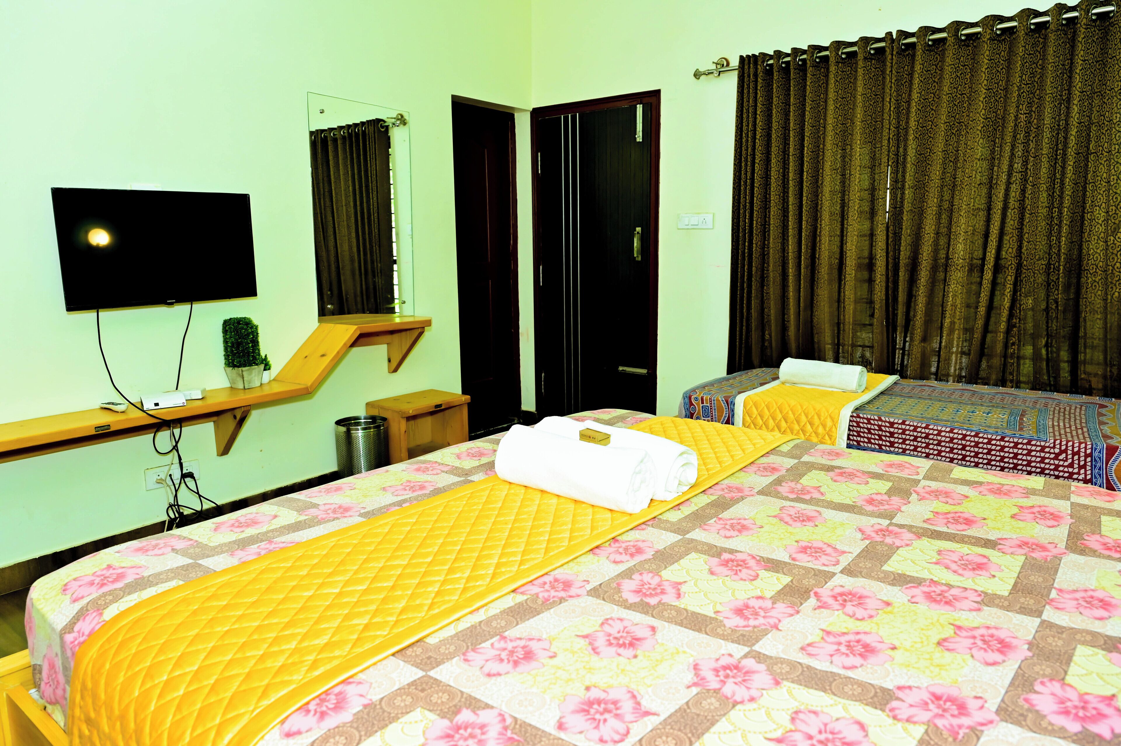 Quarto de hotel com uma cama grande, uma cama menor, uma televisão, um espelho e uma janela com cortinas.