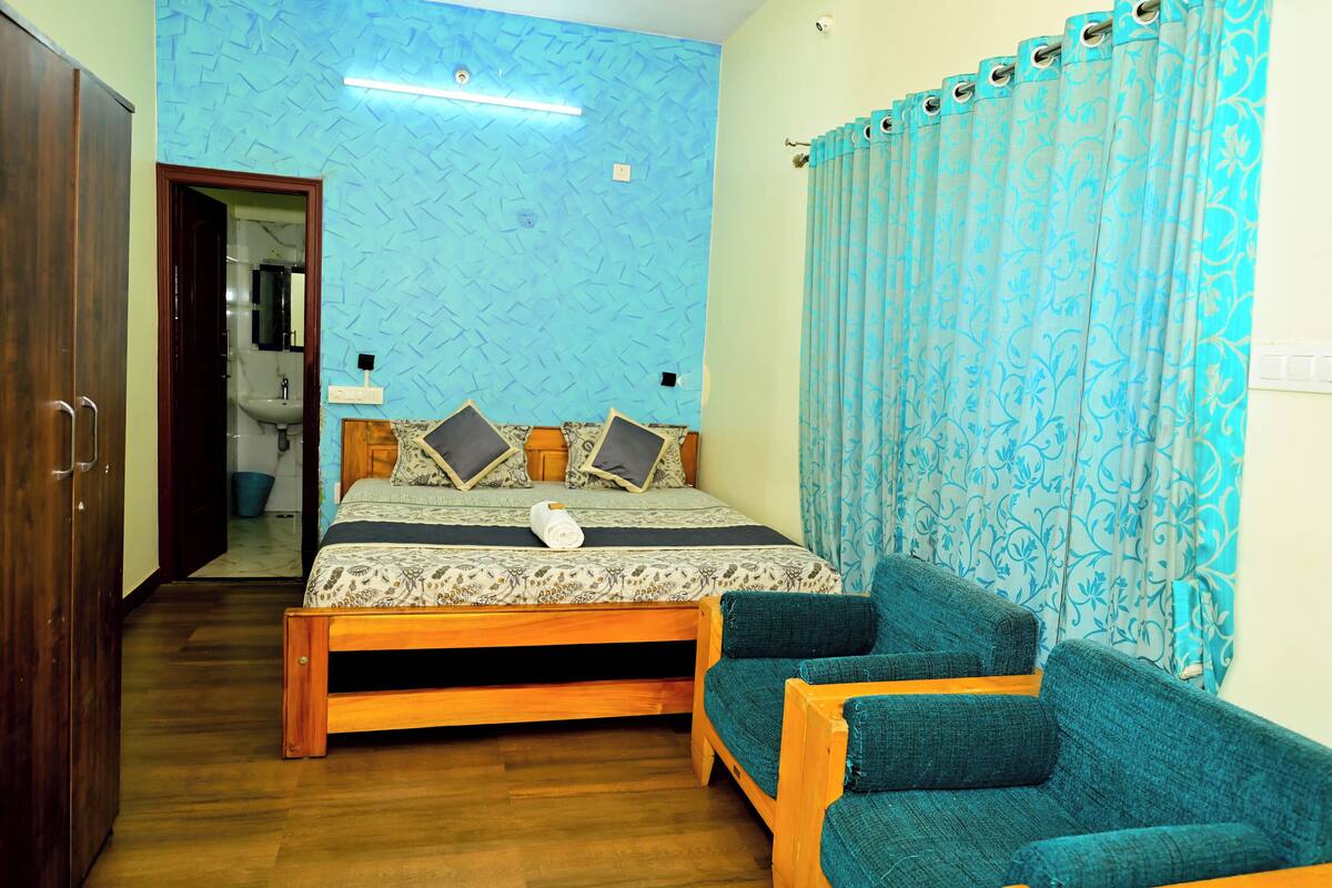 A bedroom with a bed, a wooden bench, a blue patterned curtain, and a bathroom visible through an open door.
