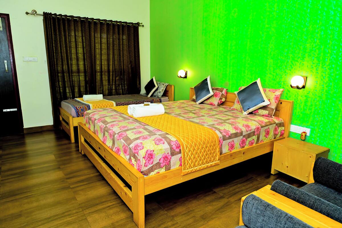A room with a large bed, two bedside tables, a small sofa, and a green accent wall.