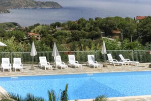A pool area with lounge chairs and umbrellas, overlooking a body of water and greenery.