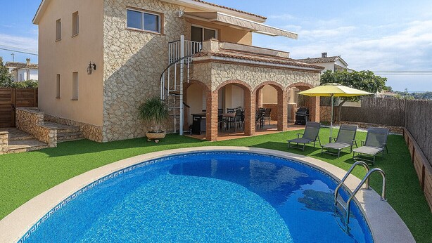 Una casa de dos pisos con fachada de piedra, piscina y mobiliario de exterior.