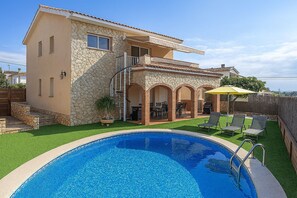 Una casa de dos pisos con fachada de piedra, piscina y mobiliario de exterior.