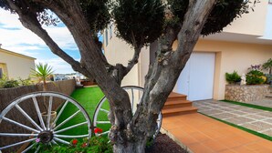Un árbol con una maceta grande con forma de rueda, un camino de piedra y una puerta.