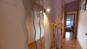 Un pasillo con un diseño de espejo único, suelo de madera y un jarrón con ramas.