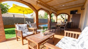Un patio al aire libre con mobiliario de madera, un paraguas amarillo y un televisor montado en la pared.