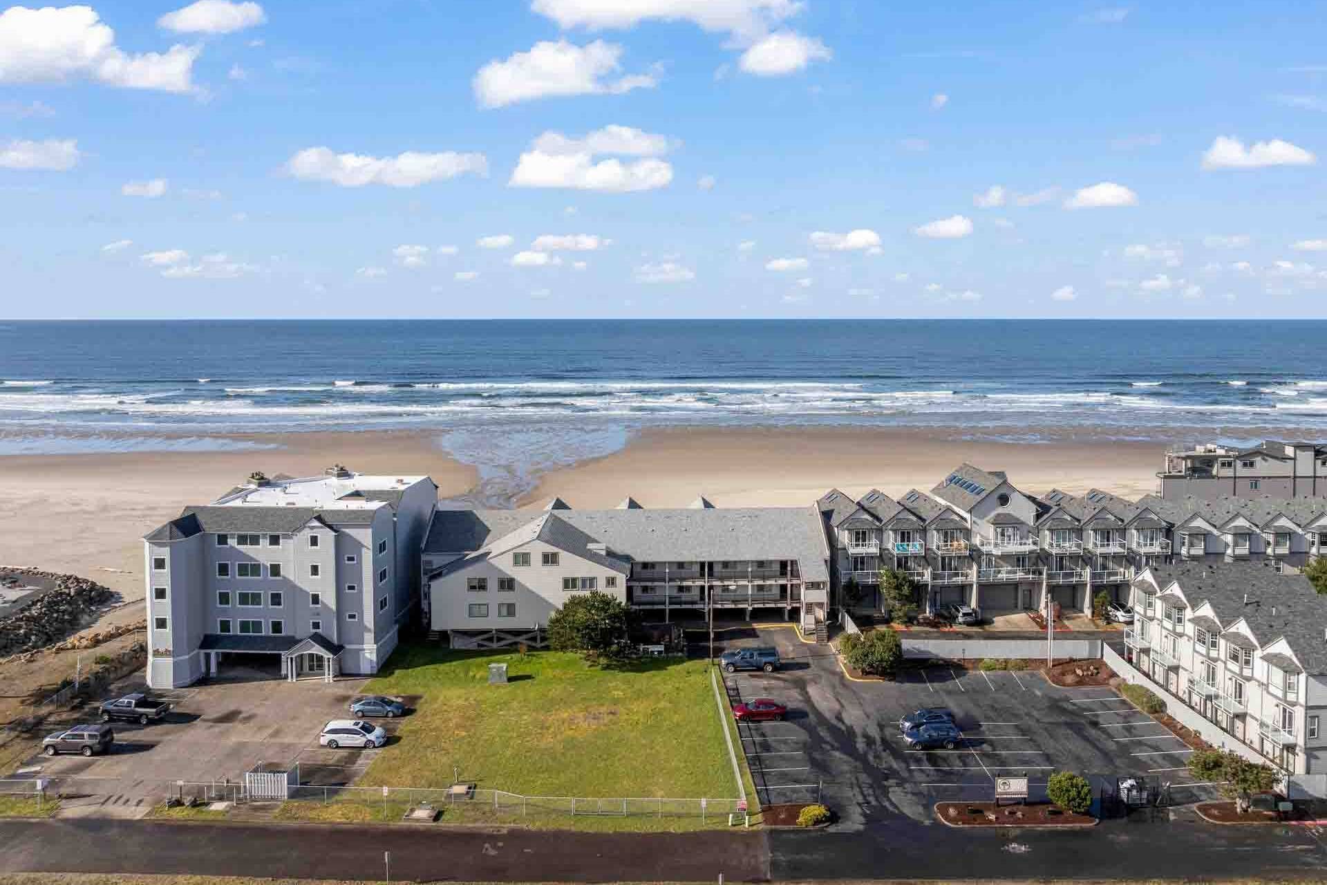 Un hotel frente al mar con varias construcciones, estacionamiento y vistas a la playa y al océano.