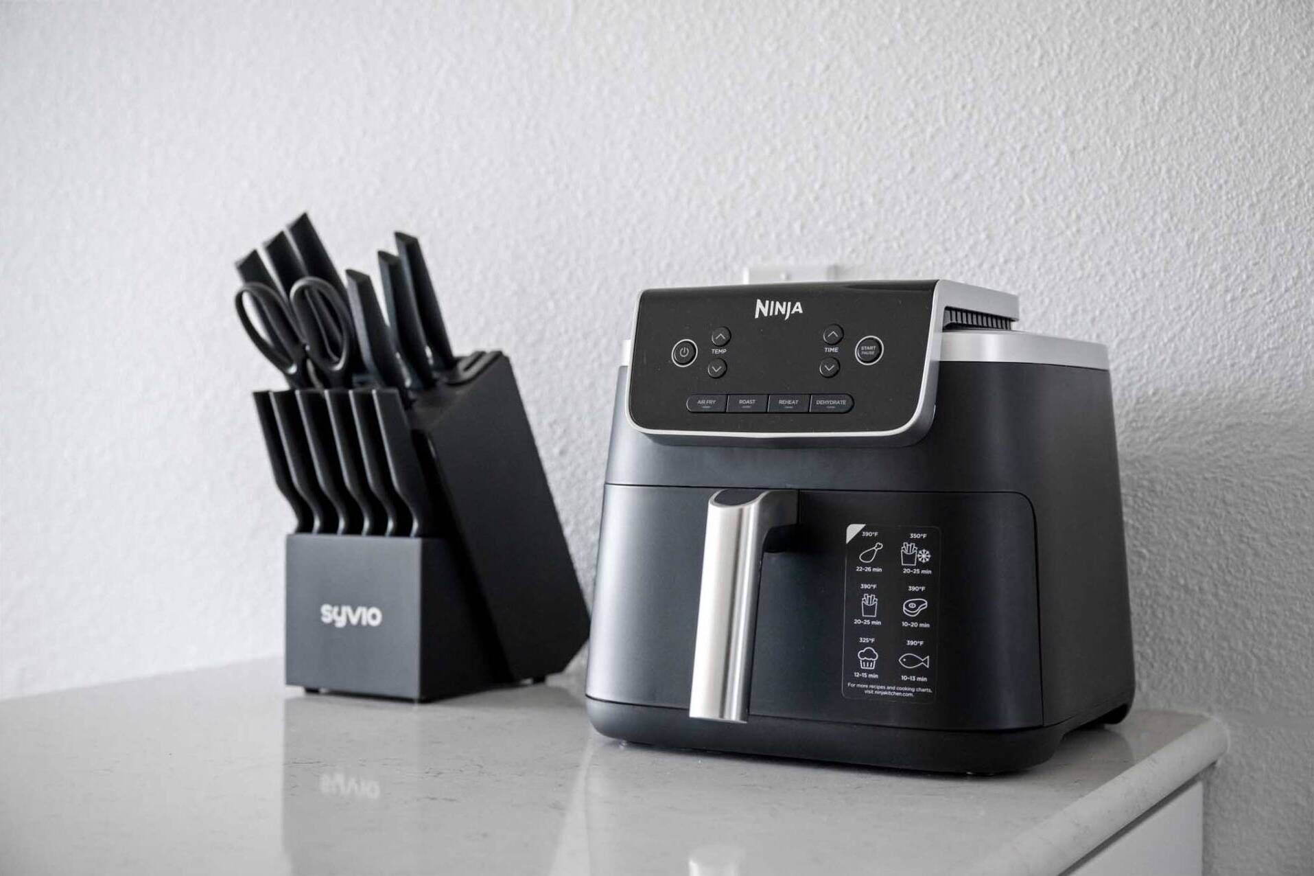 Un appareil de cuisson à air de la marque Ninja, doté d’un panneau de commande noir et d’un support à couteaux Syvyo placé à côté.