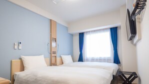Ett hotellrum med två sängar, en TV som är monterad på väggen och ett fönster med blå gardiner.