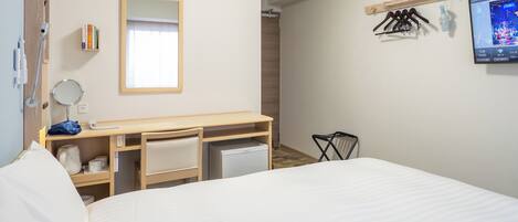 Una habitación de hotel con cama, escritorio con espejo, kitchenette pequeño, unidad de aire acondicionado, televisor y reloj de pared.