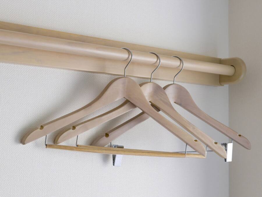 Un perchero de madera con tres perchas de madera frente a una pared lisa.
