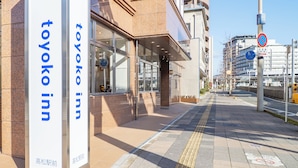 Entrada de un hotel con un letrero que dice 'Toyoko Inn' y una acera despejada.