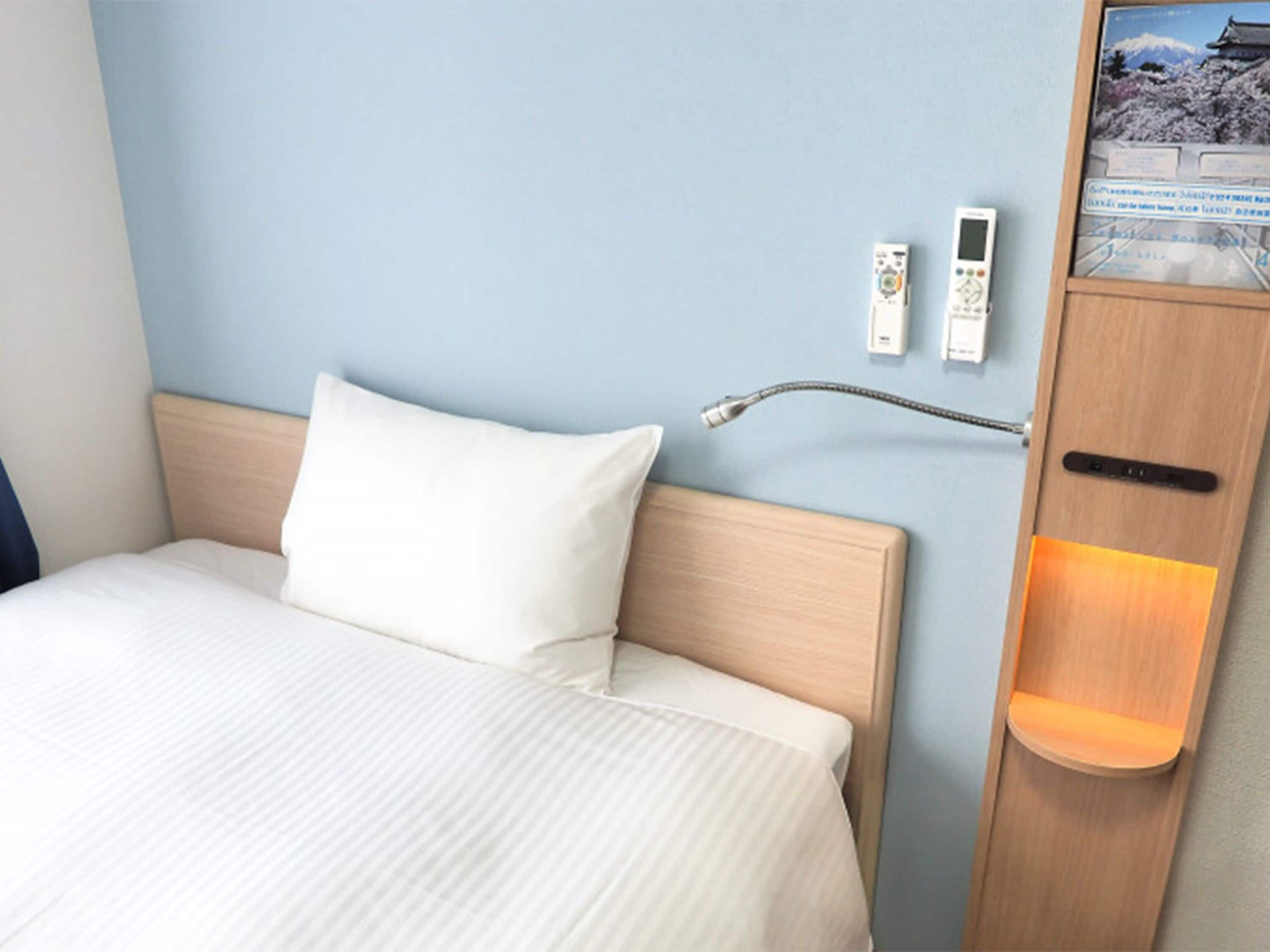 Et hotelværelse med en seng, et sengebord med lampe, en vægtelefon og en billedramme.