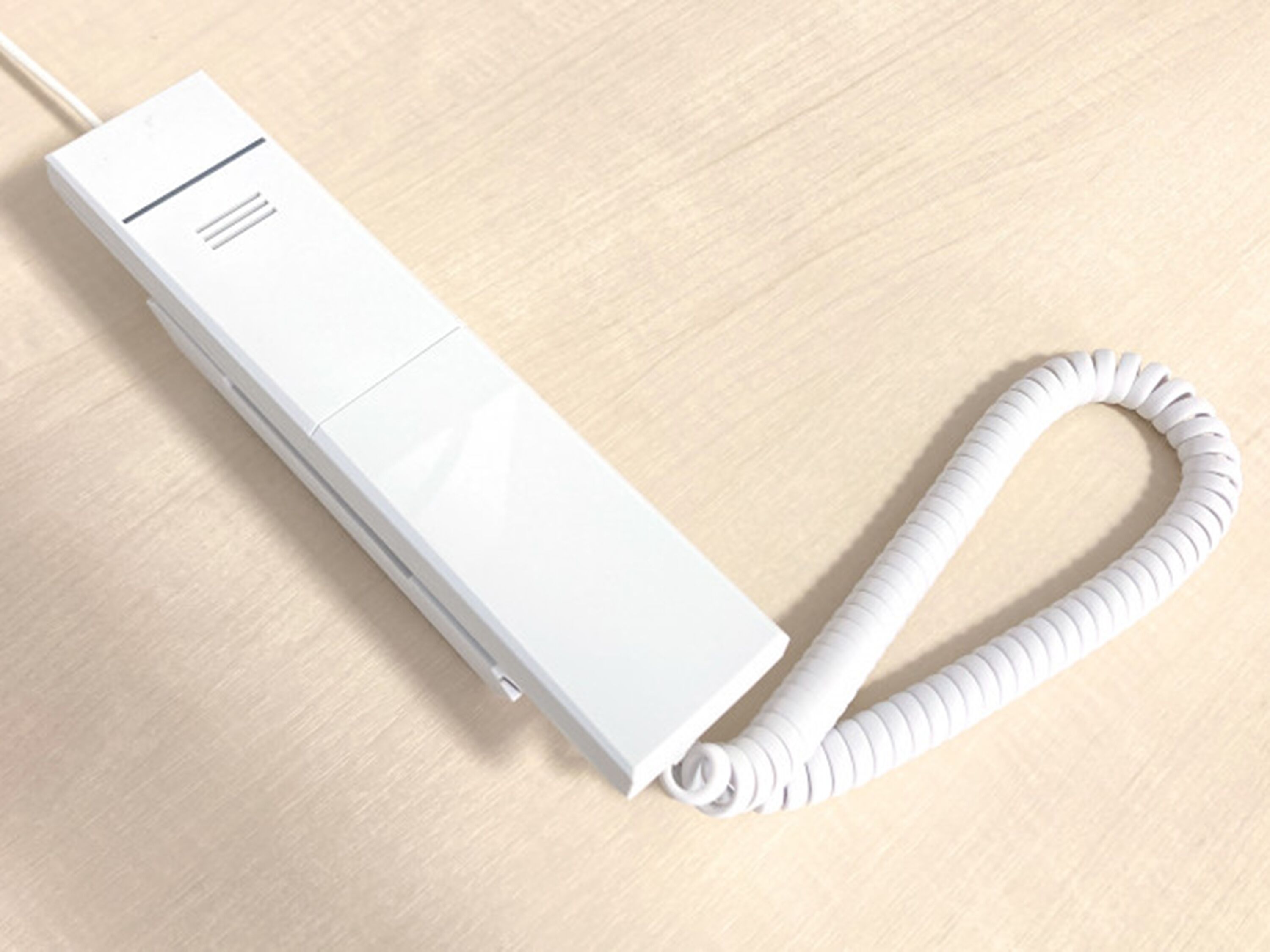 Un dispositivo electrónico blanco y rectangular con un cable enrollado sobre una superficie de madera.
