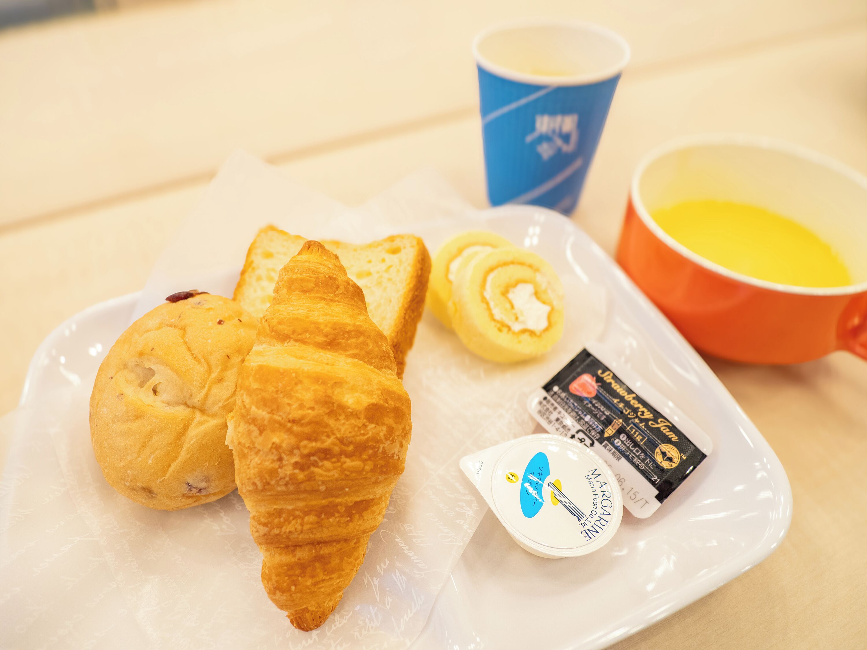 A plate with croissants, a cup, a mug, and a small container of margarine.