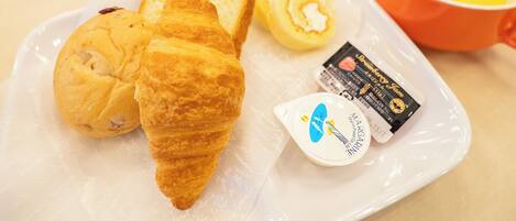 A plate with croissants, a cup, a mug, and a small container of margarine.