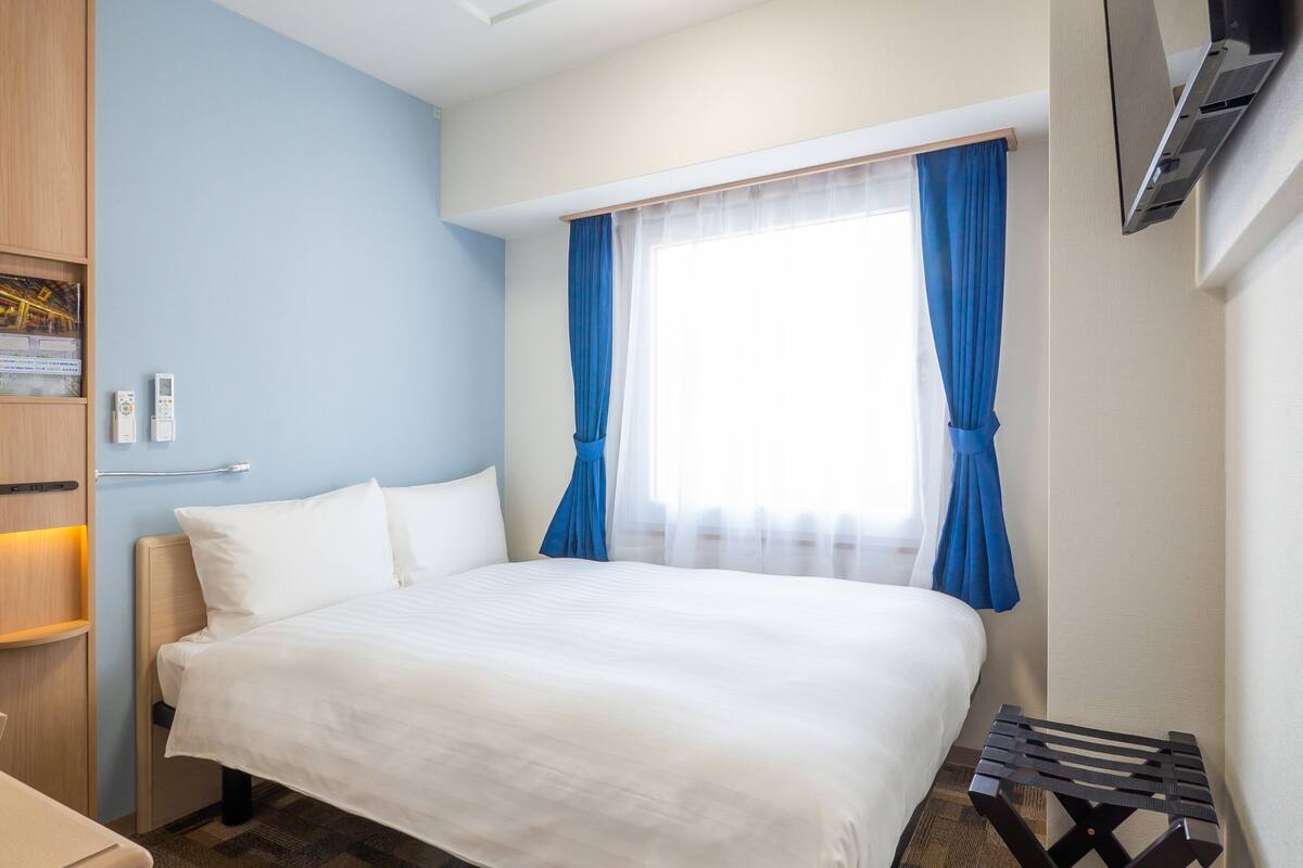 Une chambre d’hôtel avec un lit, un bureau, une télévision et une fenêtre avec des rideaux.