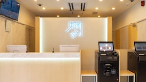 Un mostrador de recepción de hotel con un letrero de neón, una computadora y un quiosco de autoservicio.