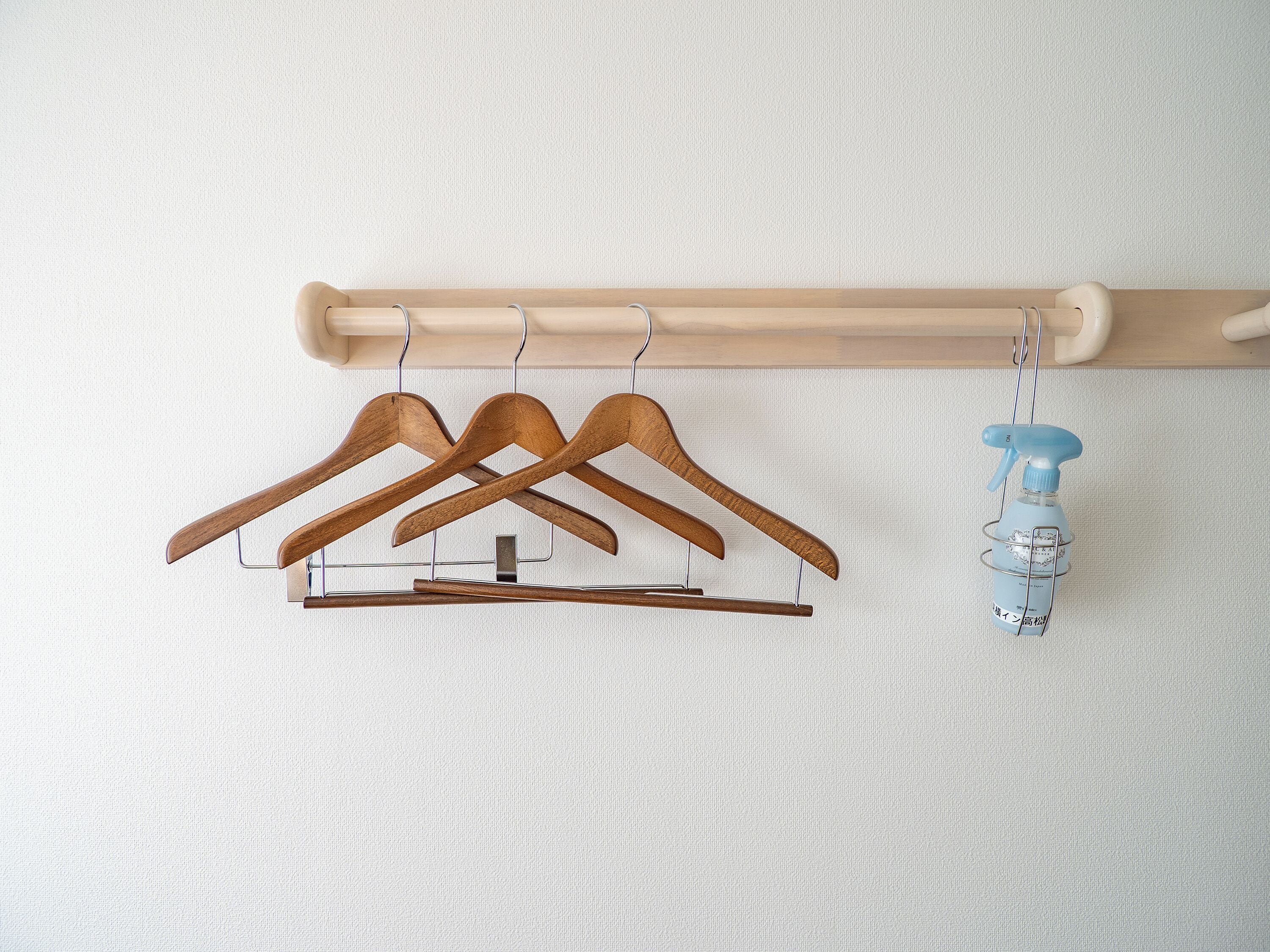 A wooden coat rack with three wooden hangers and a blue spray bottle hanging from it.