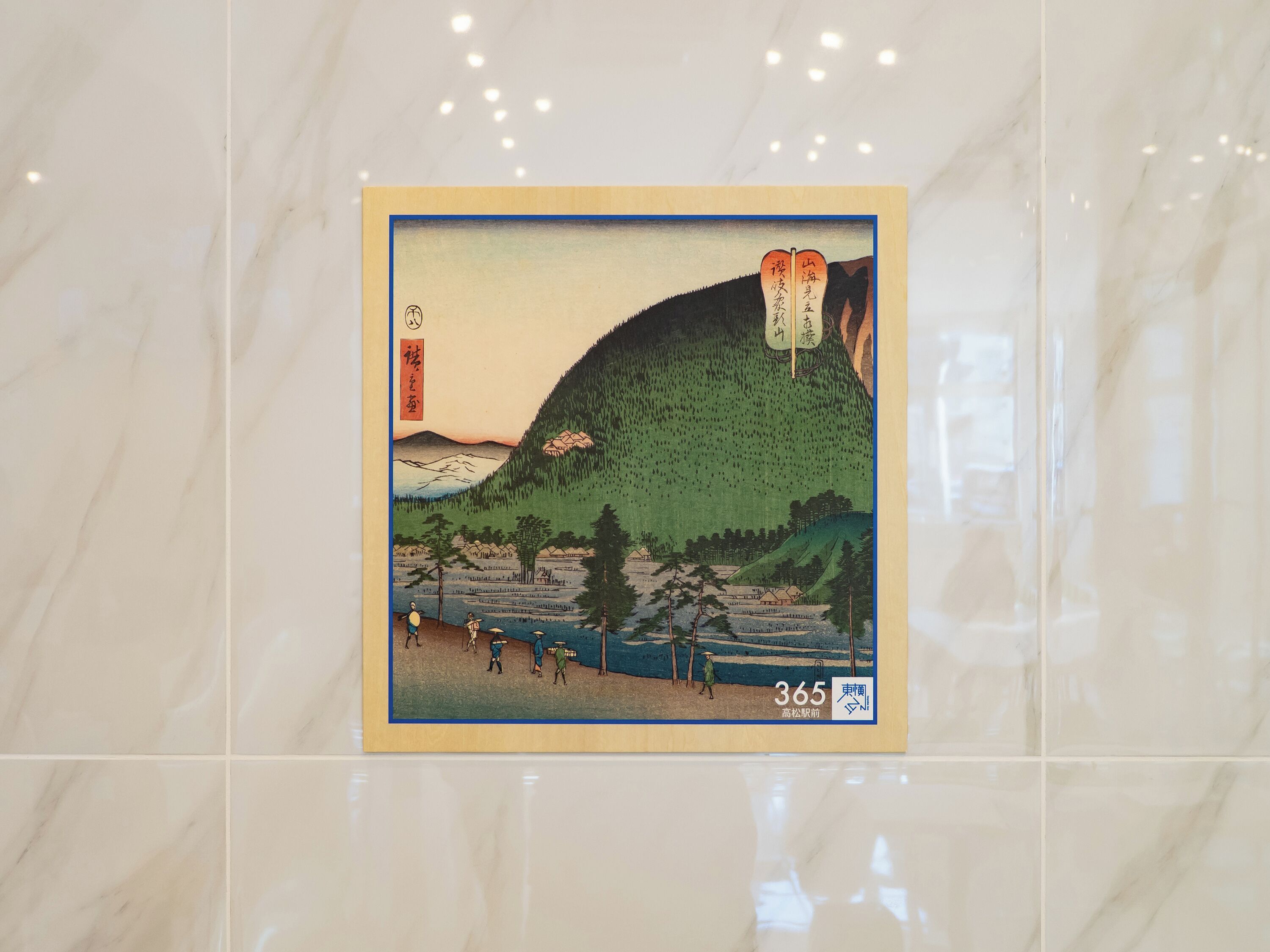 Una impresión japonesa en madera enmarco, con un paisaje montañoso y personas, sobre una superficie de mármol.