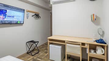 Ein Hotelzimmer mit Bett, Schreibtisch, kleinem Kühlschrank, Wandfernseher, Klimaanlage, Bücherregal und Mülleimer.