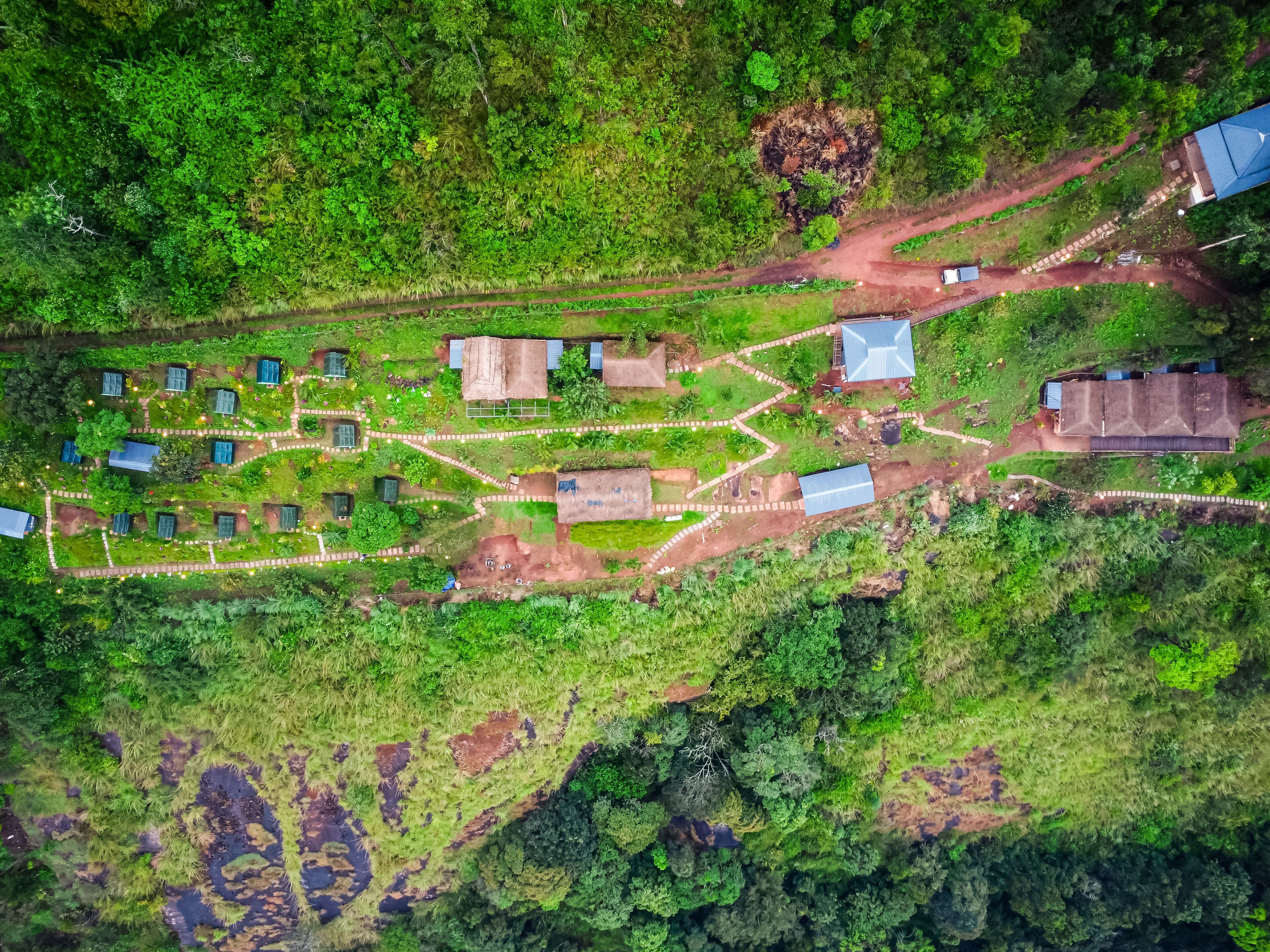 An aerial view of a rural property with several small buildings, a winding dirt road, and lush greenery.