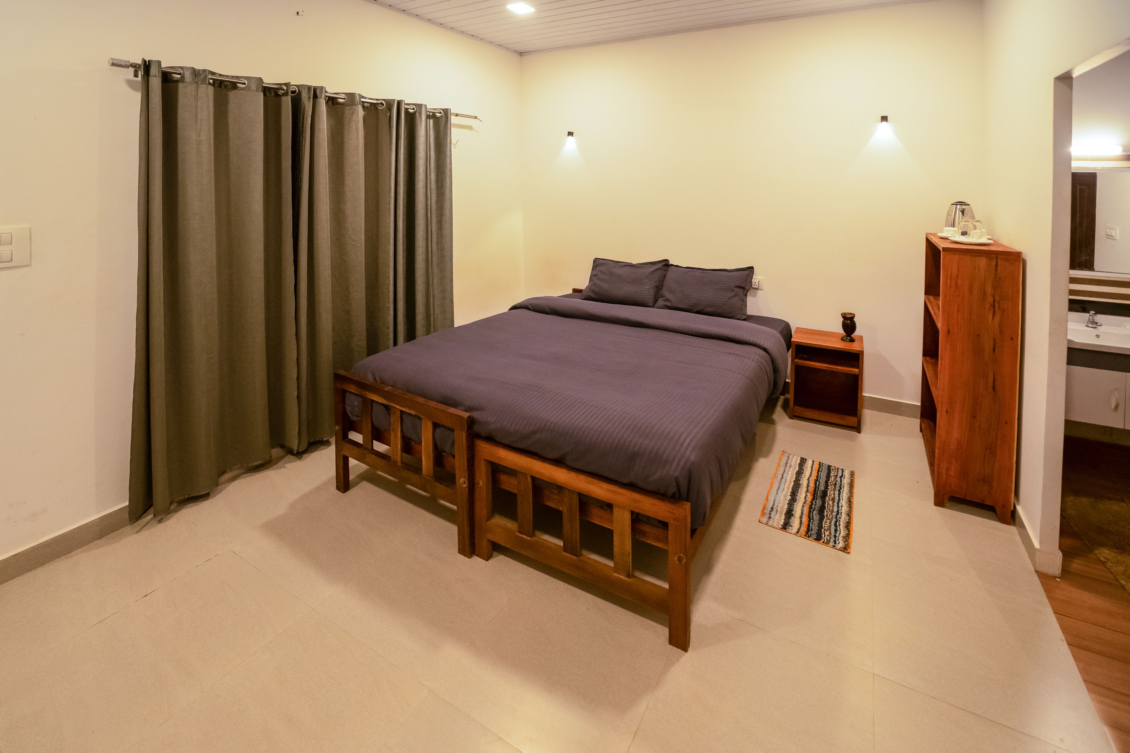 A bedroom with a bed, a nightstand, a wooden wardrobe, and a bathroom visible through an open door.